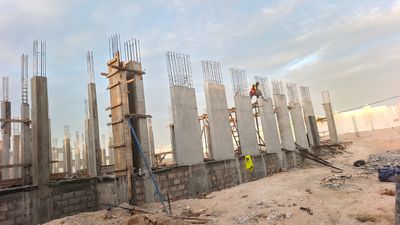 Rangée de poteaux en béton armé décoffrés, ouvrier au travail en hauteur